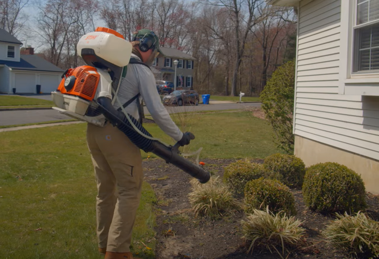 A technician using a backpack sprayer to treat shrubs outside a home as part of a Pest Control Service in Englewood.
