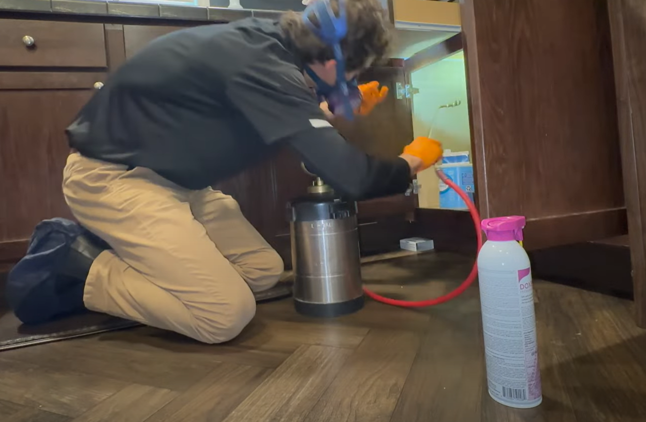 Professional applying pest control treatment under a kitchen cabinet with protective gear, showing Pest Control Service in Englewood in action.